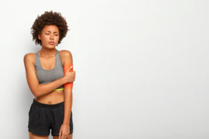 Mulher atleta com dor no braço após atividade física, ilustrando a relação entre CBD e esportes na recuperação muscular.